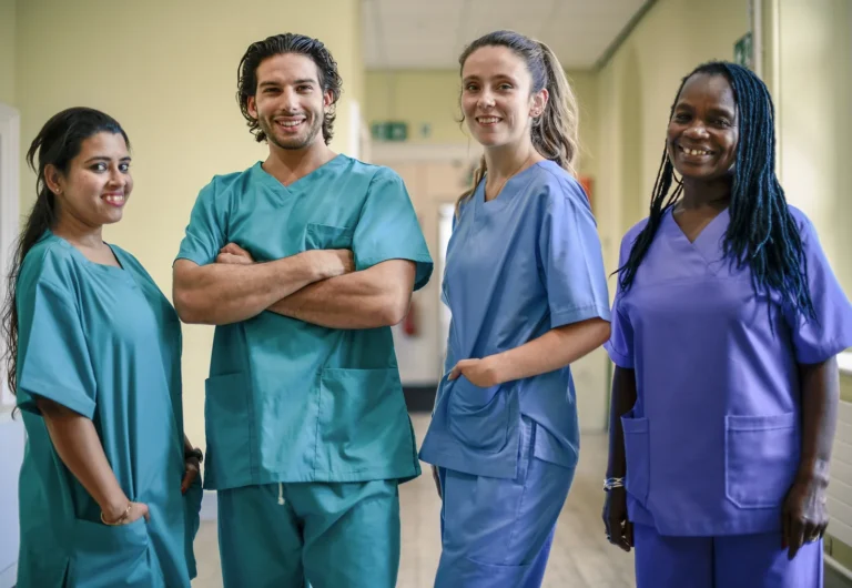 Three women and one man dressed in medical scrubs smile at the camera.