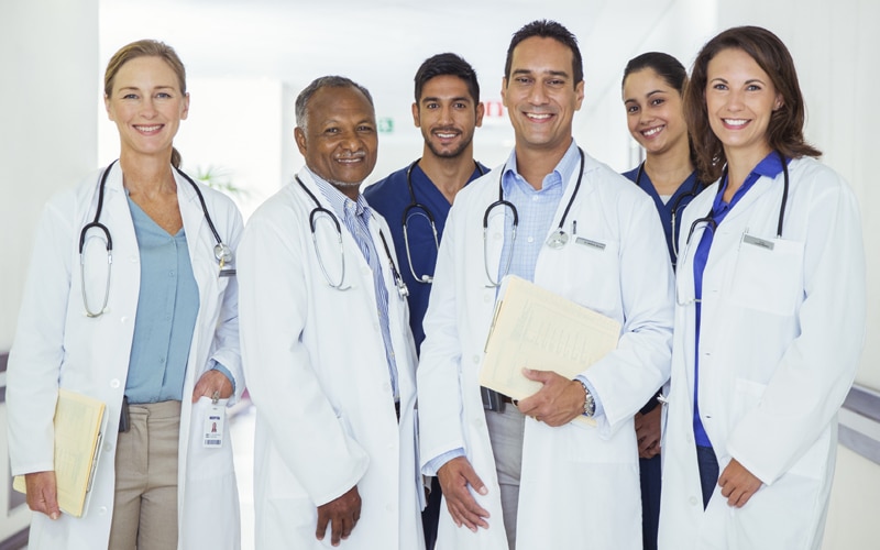 Group of six doctors in labcoats and scrubs smiling.