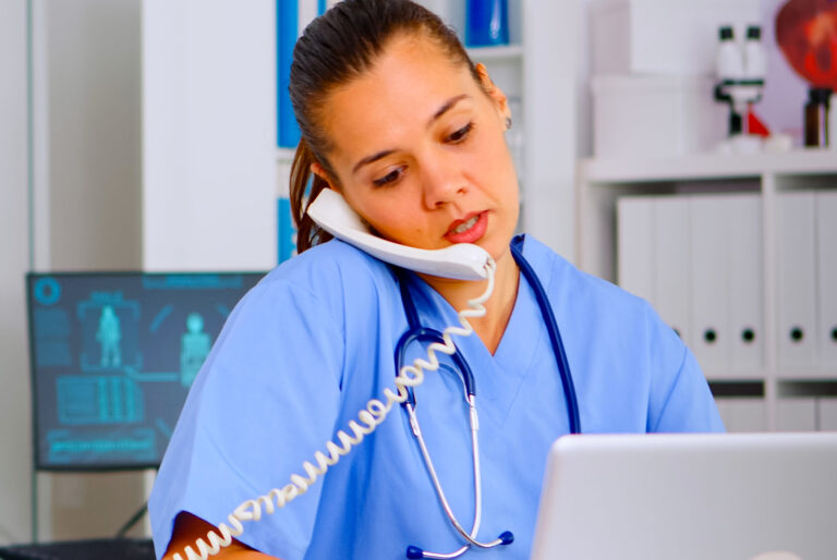 Nurse at a desk on a phone in front of a laptop